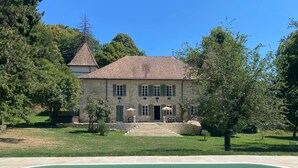 Une maison en pierre avec une piscine, entourée d’arbres et d’une pelouse bien entretenue.