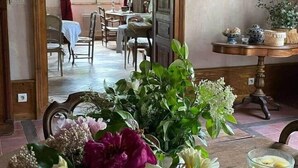 A room with a wooden table, a vase of flowers, a glass of juice, and a painting on the wall.