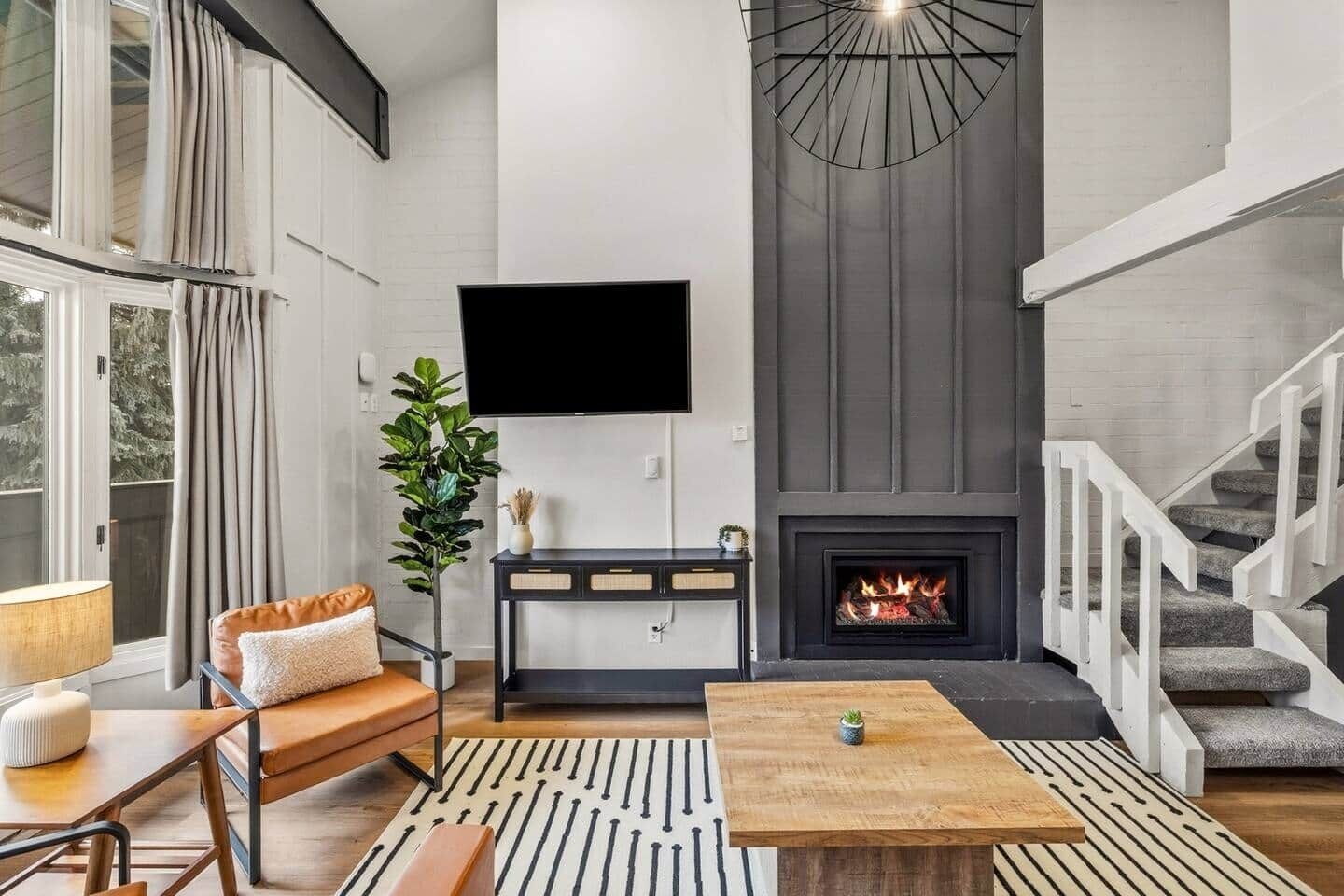Un salon moderne avec une cheminée, un téléviseur à écran plat fixé au mur et un escalier sur le côté droit.