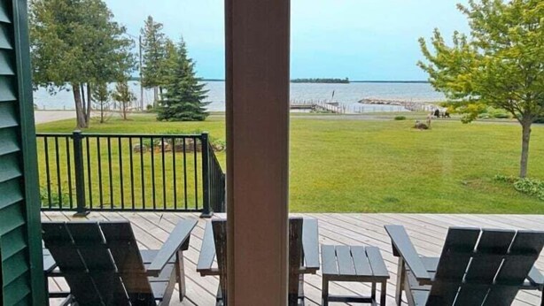 A deck with outdoor furniture, a view of the water, and a grassy area. - Hessel Bay Main Cabin : Idyllic Les Cheneaux Islands waterfront cabin sleeps 8 (Hessel)