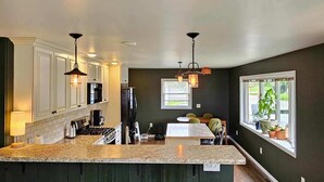 A spacious kitchen with a large island, dark wooden cabinets, and pendant lighting. - Hessel Bay Main Cabin : Idyllic Les Cheneaux Islands waterfront cabin sleeps 8 (Hessel)