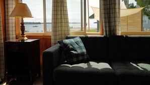 A room with a sofa, a lamp, and a view of a body of water through large windows. - Hessel Bay Cabin 1:  Lake Huron waterfront resort cabin sleeps 2. (Hessel)