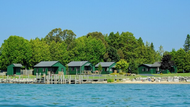 A row of green cabins by a lake with a dock, surrounded by trees. - Hessel Bay Cabin 2:  Lake Huron waterfront resort cabin sleeps 2. (Hessel)