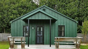 A green wooden cabin with a front door, two windows, and a porch with benches. - Hessel Bay Cabin 2:  Lake Huron waterfront resort cabin sleeps 2. (Hessel)
