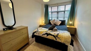 A bedroom with a bed, bedside lamps, a dresser, a mirror, and a window with curtains. - 2br city side apartment (Belfast)