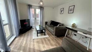 A living room with a sofa, a coffee table, a TV, and a balcony with curtains. - 2br city side apartment (Belfast)