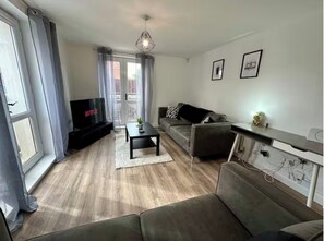 Ein Wohnzimmer mit einer Couch, einem Couchtisch, einem Fernseher und einem Balkon mit Vorhängen.