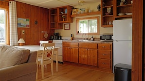 A kitchen with wooden cabinets, a refrigerator, a microwave, a sink, and a dining area with a table and chairs. - Hessel Bay Cabin #4:  Lake Huron waterfront cabin sleeps 4. (Hessel)