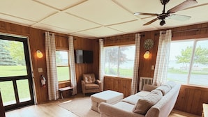 A room with a wooden floor, a sofa, a chair, a television, and a ceiling fan. - Hessel Bay Cabin #4:  Lake Huron waterfront cabin sleeps 4. (Hessel)