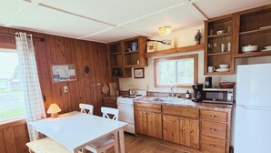 A kitchen with wooden cabinets, a white refrigerator, a stove, and a dining table with chairs. - Hessel Bay Cabin #4:  Lake Huron waterfront cabin sleeps 4. (Hessel)