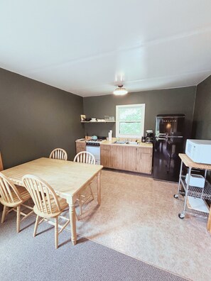 A compact kitchen with a dining table and chairs, a refrigerator, and a microwave.