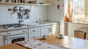 Eine Küche mit Gasherd, weißen Schränken, einem Holztisch mit Blumenmuster und einer Pendelleuchte.