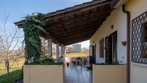 Eine überdachte Terrasse mit Tisch und Stühlen, Blick auf die Landschaft und ein Gebäude im Hintergrund.