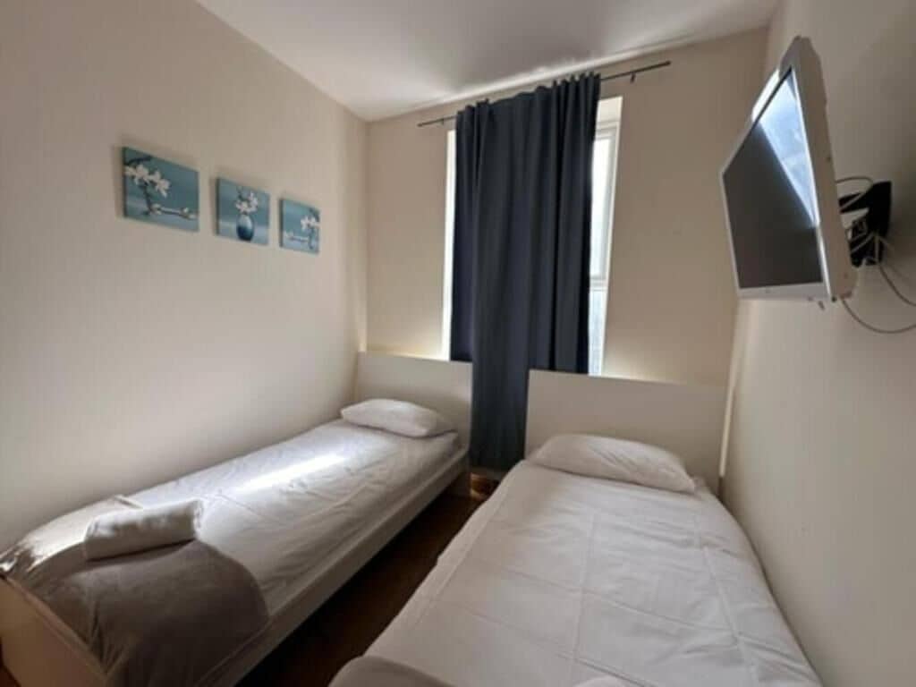 Una habitación con dos camas individuales, una ventana con cortinas y obras de arte colgadas en la pared.