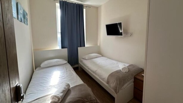 Ein kleines, sauberes Zimmer mit zwei Einzelbetten, einem Fernseher und einem Fenster mit Vorhängen.