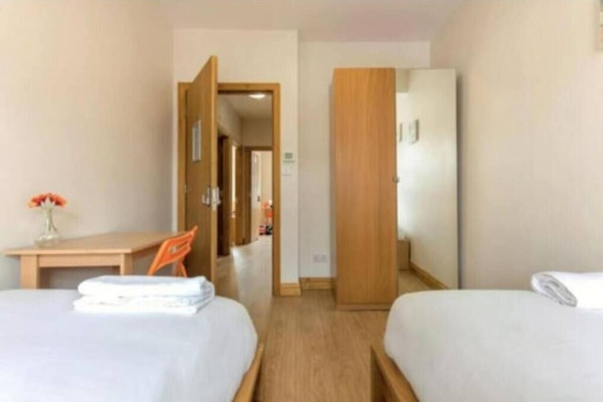 Une chambre d’hôtel avec deux lits, un bureau avec une chaise et une armoire en bois.