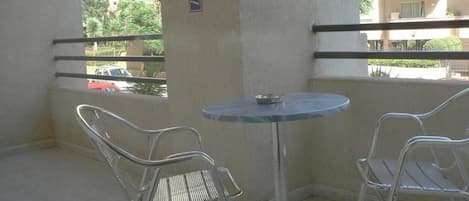A balcony with two metal chairs and a small round table, overlooking a residential area with buildings and trees.