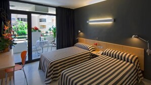 A hotel room with two beds, a desk, a chair, a balcony with a table and chairs, and a view of the outside. - Hotel Nautico (Santa Cruz de Tenerife)