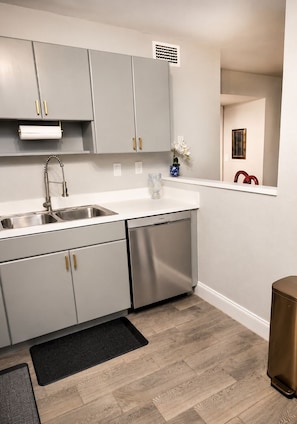 A modern kitchen with grey cabinets, stainless steel appliances, and a wooden floor.