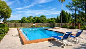Ein rechteckiger Pool mit Holzterrasse, umgeben von einem Holzzaun, und zwei Liegestühle mit blauen Kissen.
