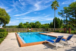 A rectangular swimming pool with a wooden deck, surrounded by a wooden fence, and two lounge chairs with blue cushions.