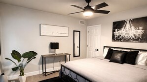 Ein Schlafzimmer mit einem Bett, einem Deckenventilator, einem Schreibtisch, einem Stuhl, einer Pflanze und einer Pendelleuchte.