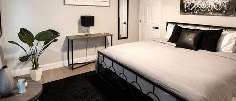 Un dormitorio con cama, ventilador de techo, escritorio, silla, planta y candelabro.