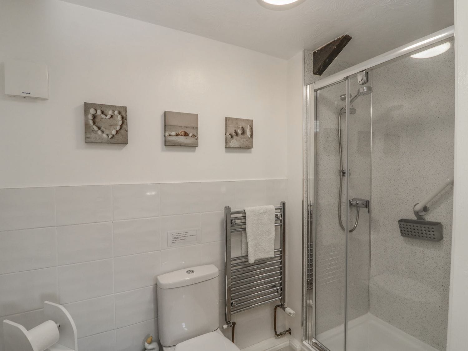 Un baño con ducha de vidrio, azulejos blancos y tres obras de arte enmarcadas en la pared.