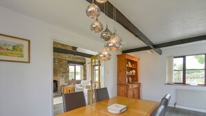 Ein Essbereich mit Holztisch, Stühlen und einer Chandelier. Eine Steinwand und ein Fenster mit Jalousien sind zu sehen.
