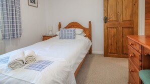 Ein Schlafzimmer mit einem hölzernen Bett, einem Nachttisch mit Lampe sowie einer Holzkommode und einer Holztür.