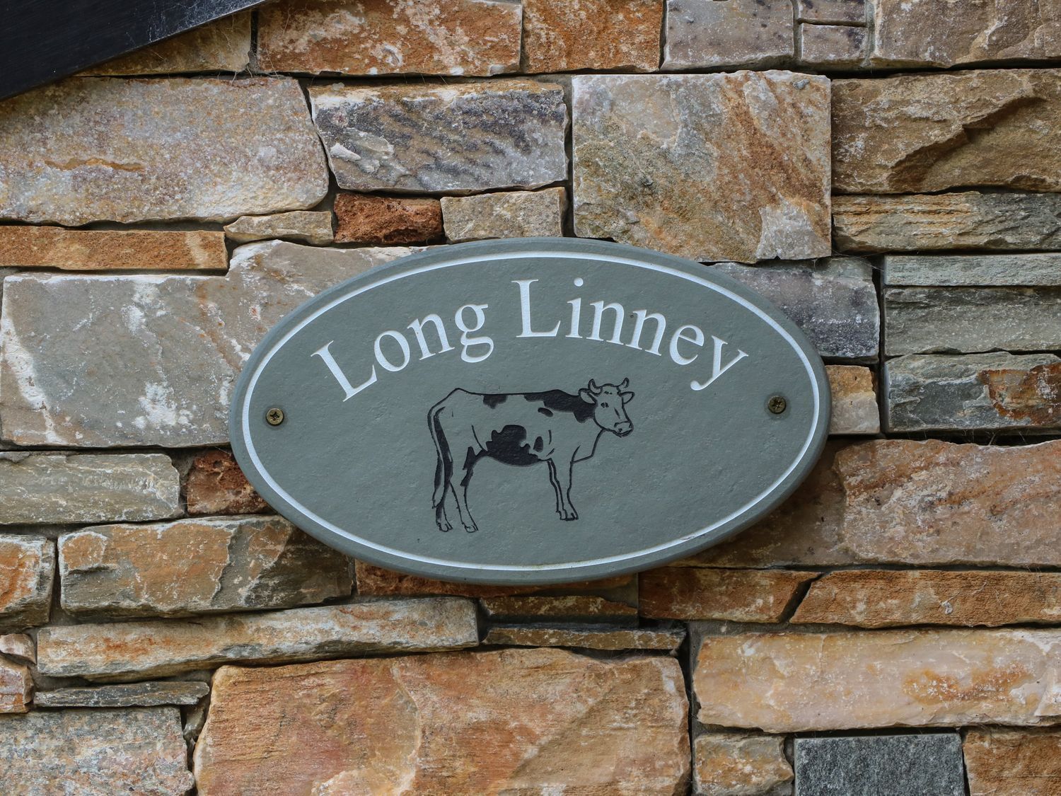A stone wall with a sign that reads 'Long Linney' and features a cow illustration.