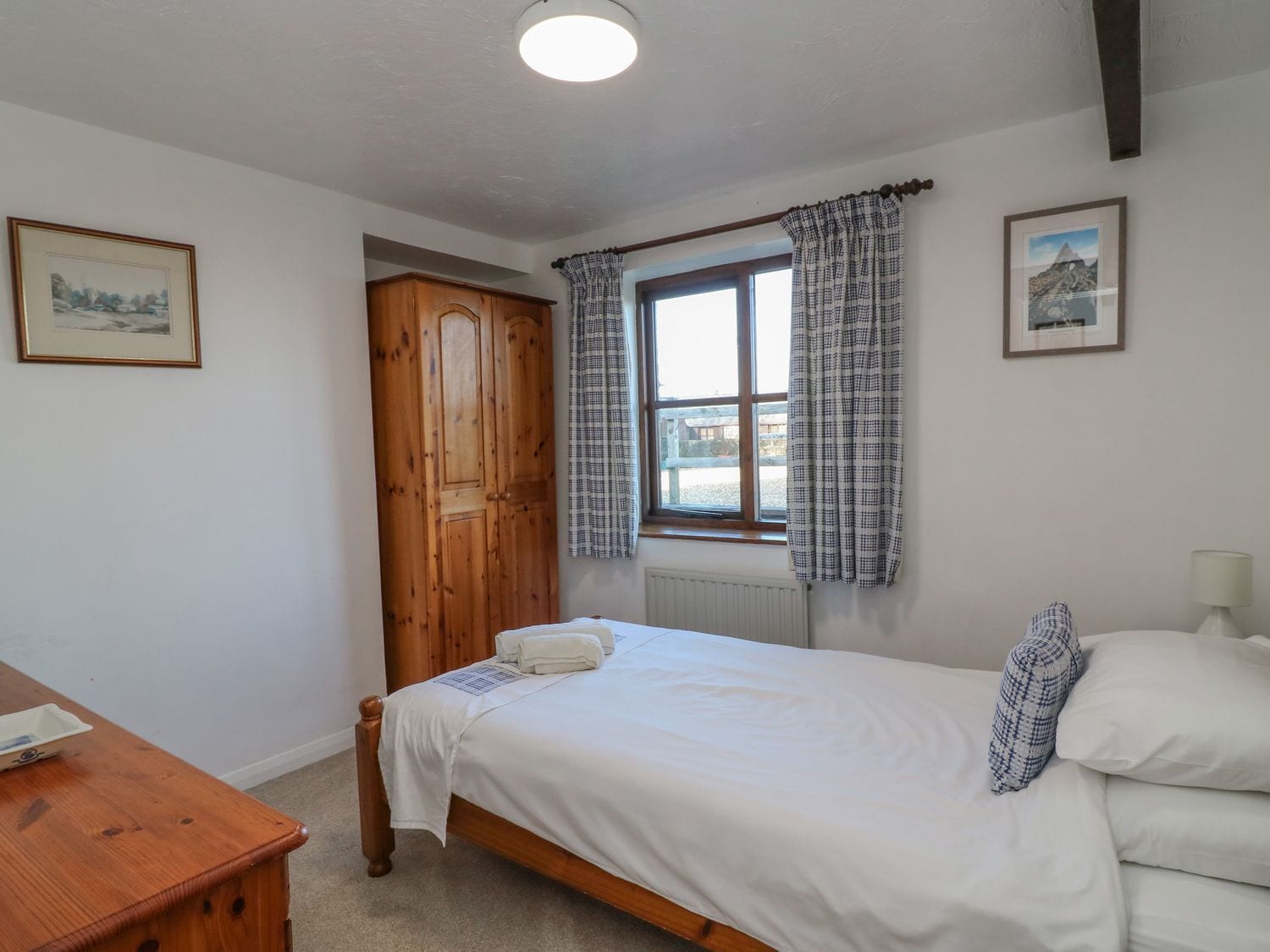A bedroom with a wooden bed, a window with curtains, a radiator, and a wooden wardrobe.