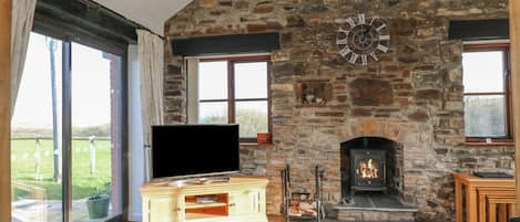 A stone fireplace, a television on a wooden cabinet, and a sofa in a room with large windows.