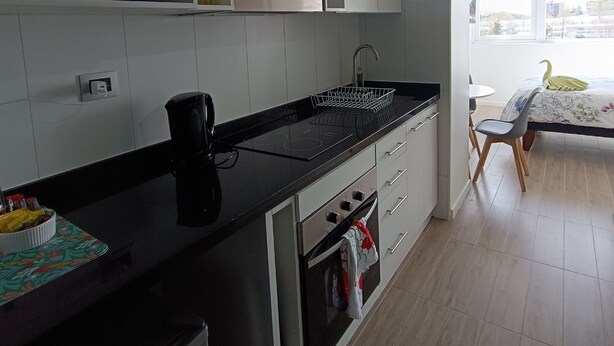 Une cuisine moderne avec des meubles blancs, un plan de travail noir, un four à micro-ondes encastré et un coin repas comprenant une table et des chaises.