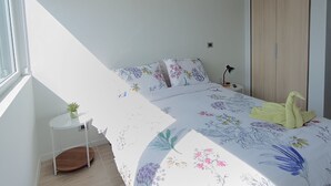 Une chambre à coucher avec un lit, une armoire, une petite table avec une lampe et une fenêtre.