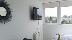 Une chambre d’hôtel avec un lit, un téléviseur fixé au mur, un miroir rond, une petite table et une chaise.