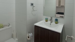 Une salle de bain comprenant des toilettes, une douche, un lavabo avec un miroir et une poubelle.