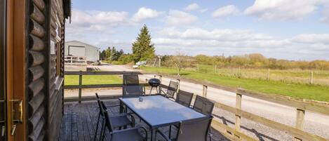 A deck with a table and chairs, a view of the countryside, and a building in the background.
