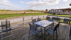 A deck with outdoor seating, a view of the countryside, and a building in the background. - Lavender Lodge (Evesham)