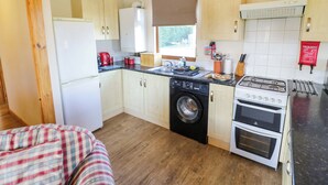 A compact kitchen with a washing machine, a stove, and a refrigerator. - Lavender Lodge (Evesham)