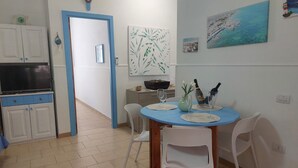 Un coin repas avec une table bleue, des chaises blanches et une cuisine en arrière-plan.
