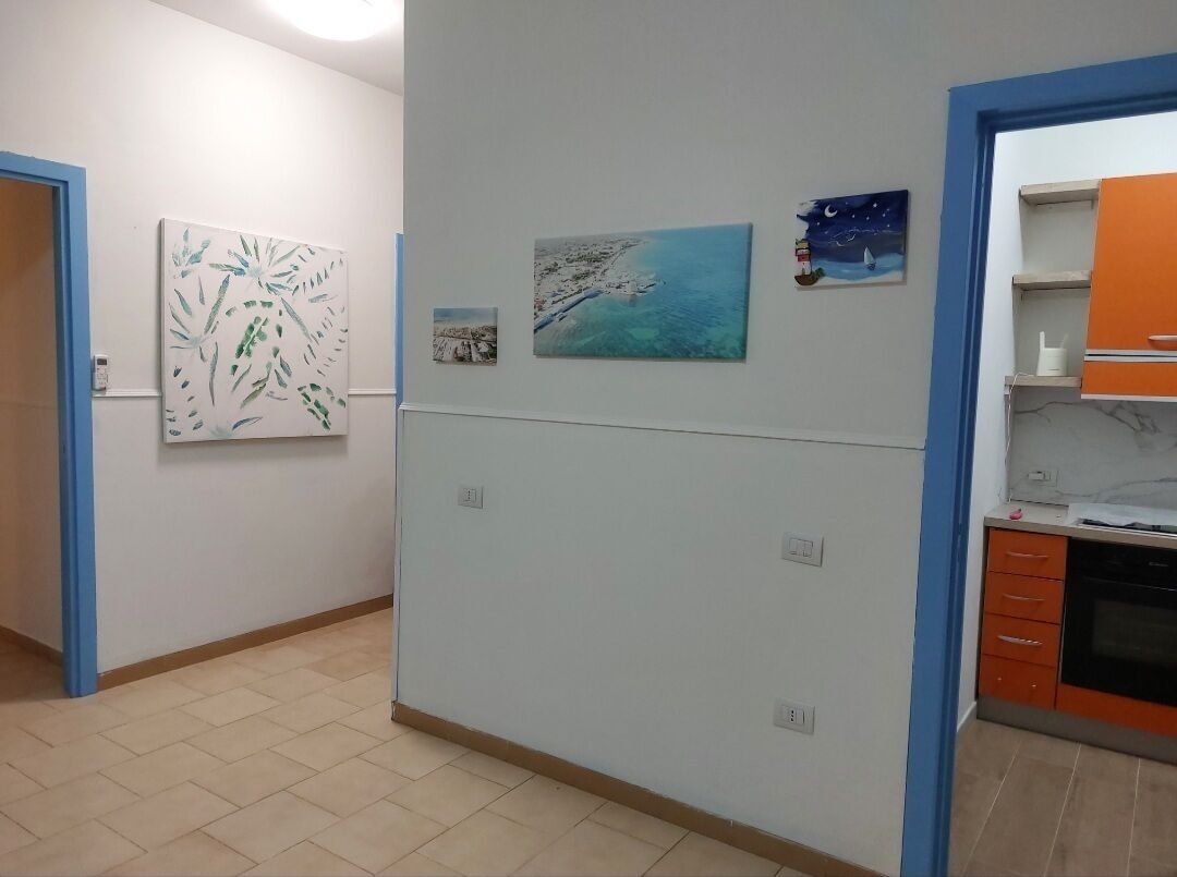A hallway with artwork on the walls, a kitchen area with orange cabinets, and a tiled floor.