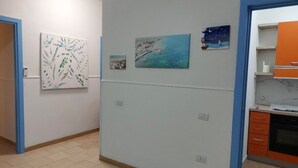 Un couloir orné de tableaux, une cuisine avec des meubles de couleur orange et un sol carrelé.