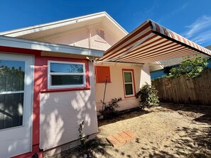A residential building with a red and white exterior, a covered patio, and a wooden fence. - Adorable 2-bedroom bungalow with AC in Daytona Beach, walking distance to beach (Daytona Beach)