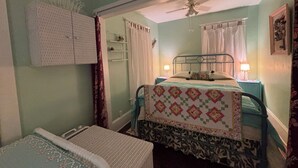 Un dormitorio con una cama individual, una mesita de noche, un ventilador de techo y una ventana con cortinas.
