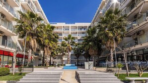 A multi-story hotel with a central courtyard, palm trees, and a blue pool. - Beachfront Apartment with Pool Access by PikHost (Shëngjin)