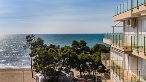 A coastal building with a balcony overlooking the sea, trees in the foreground, and a clear sky. - Beachfront Apartment with Pool Access by PikHost (Shëngjin)