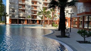 A modern hotel with a swimming pool, palm trees, and a clear blue sky. - Beachfront Apartment with Pool Access by PikHost (Shëngjin)