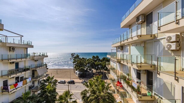 A coastal building with balconies overlooking the sea, air conditioning units, and a parking area with cars. - Beachfront Apartment with Pool Access by PikHost (Shëngjin)