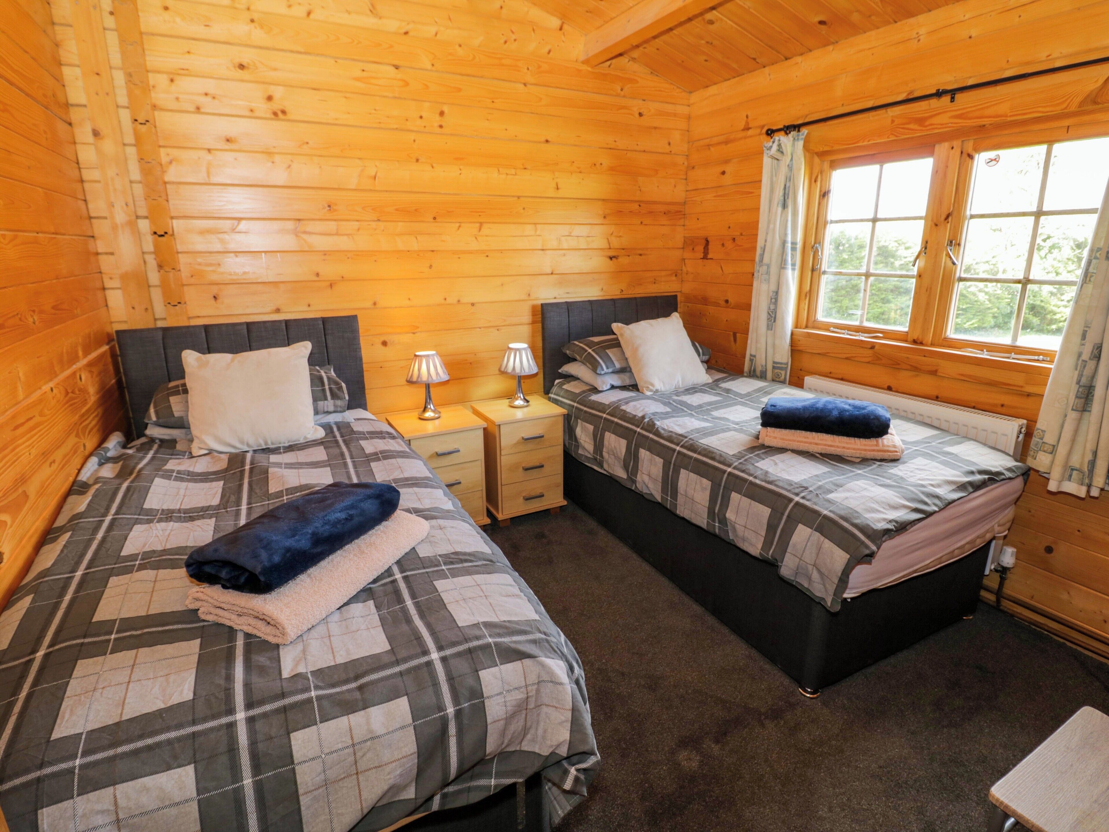 Een kamer in chaletstijl met twee bedden, houten wanden, een raam met gordijnen en een nachtkastje met een lamp.